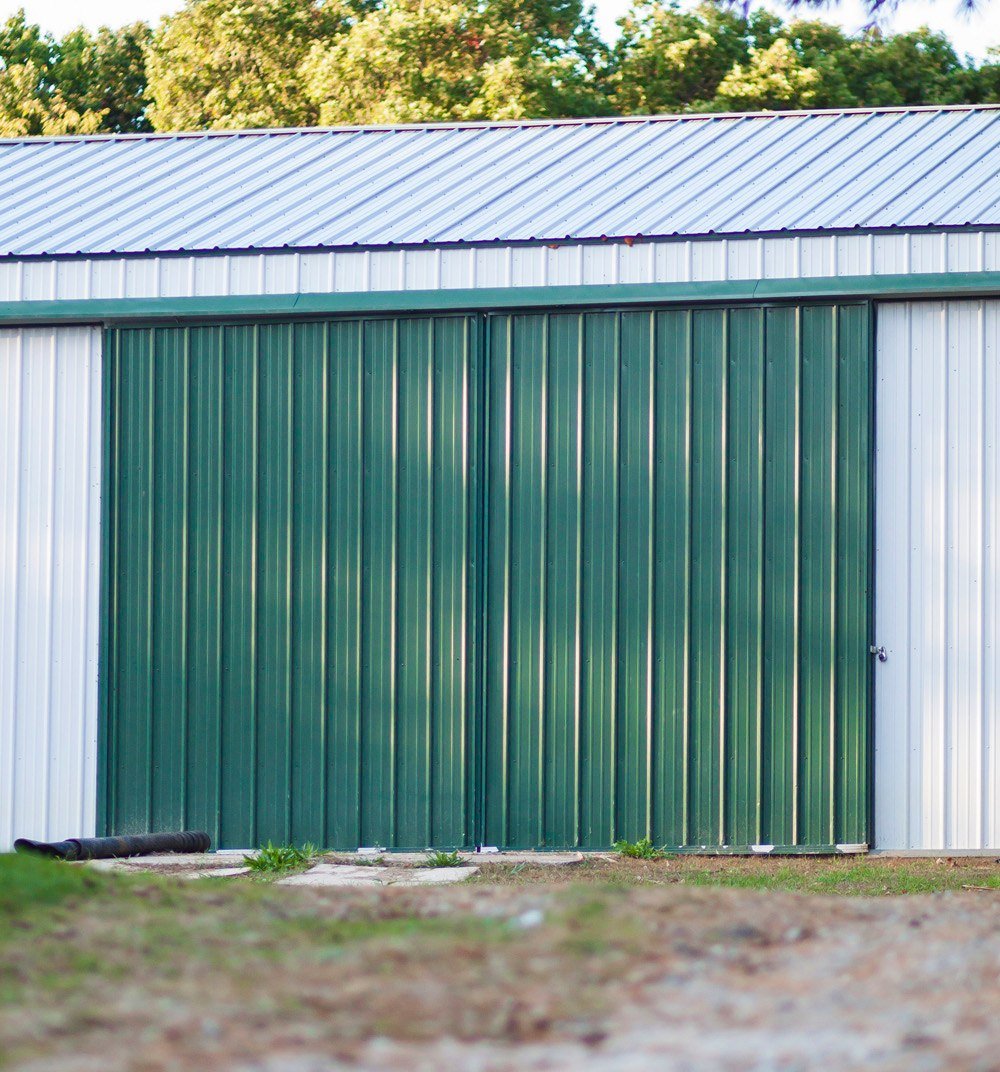 Crimson red pole barn workshop with a white roof, a large white door, and a small white door