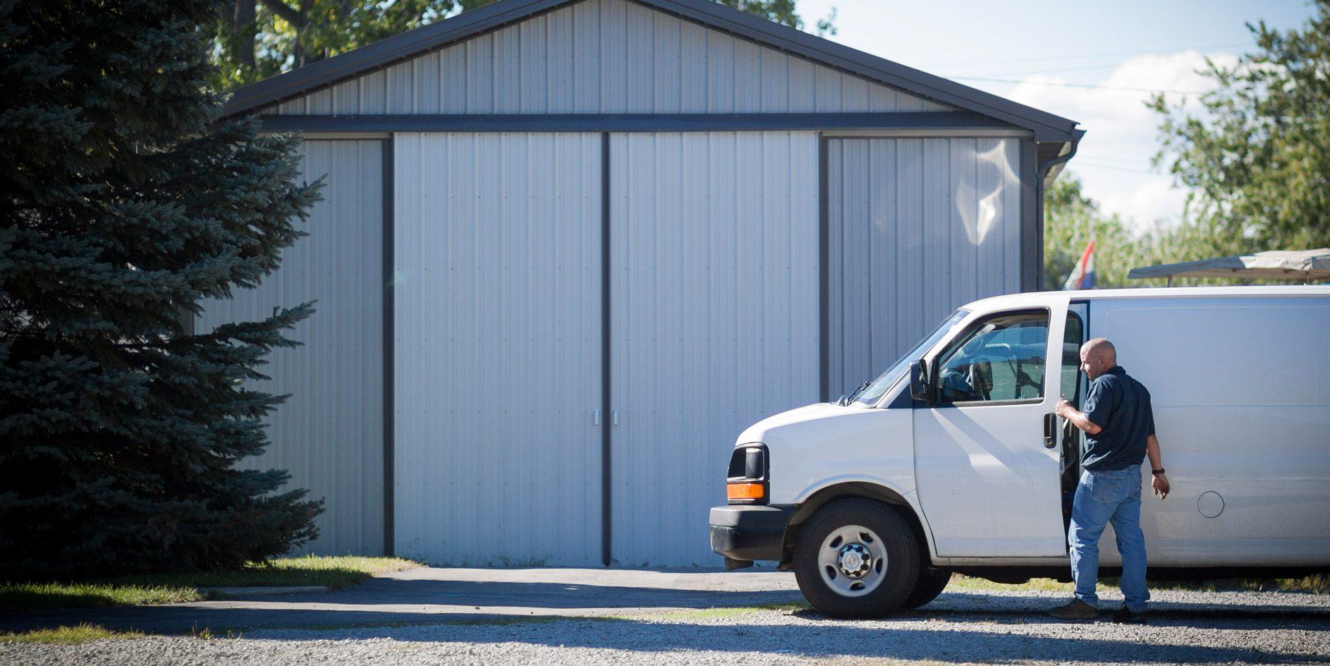 Tan pole barn garage with an evergreen roof, a large white door, and a small white door
