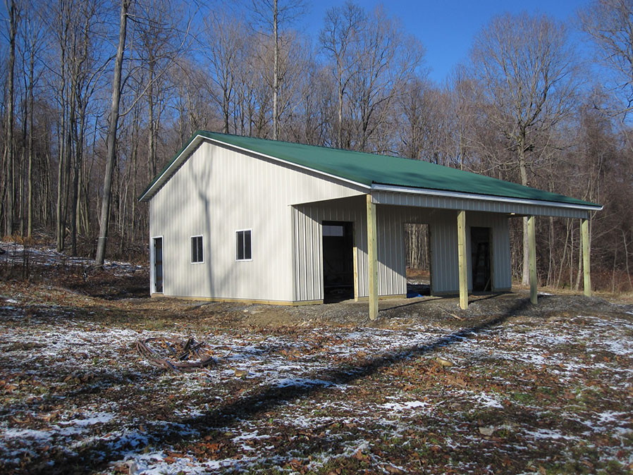 Crimson red pole barn workshop with a white roof, a large white door, and a small white door